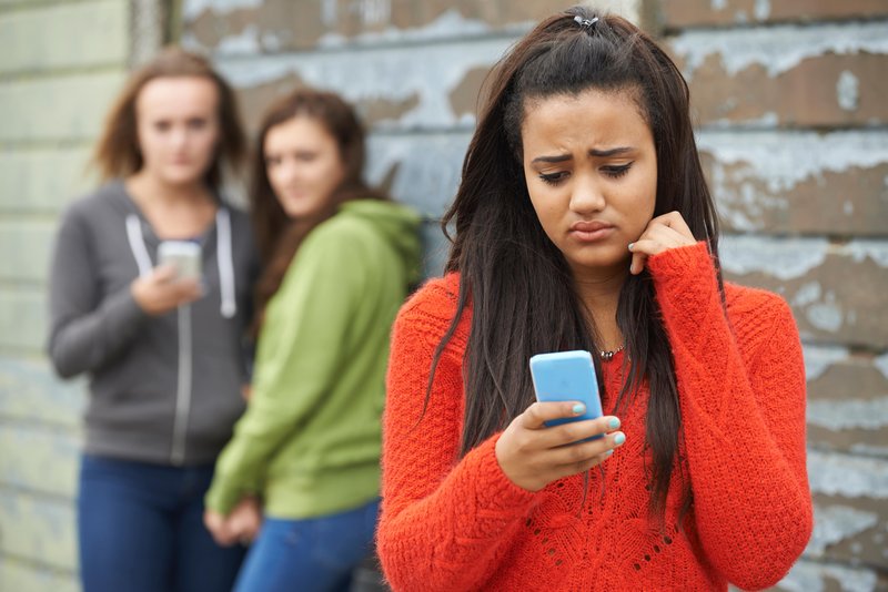 Cybermobbing - Schülerin schaut traurig auf ihr Handy
