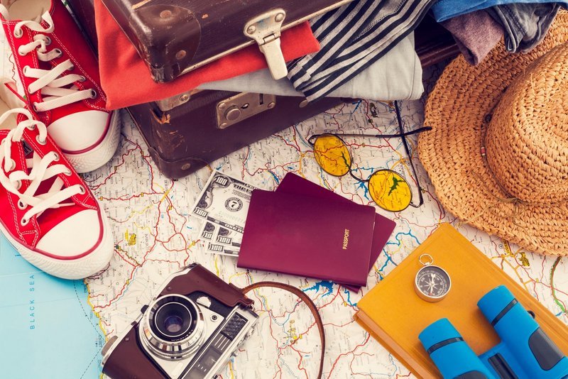 Gegenstände wie Schuhe, eine Kamera und zwei Reisepässe für ein Reise liegen auf einer Karte.