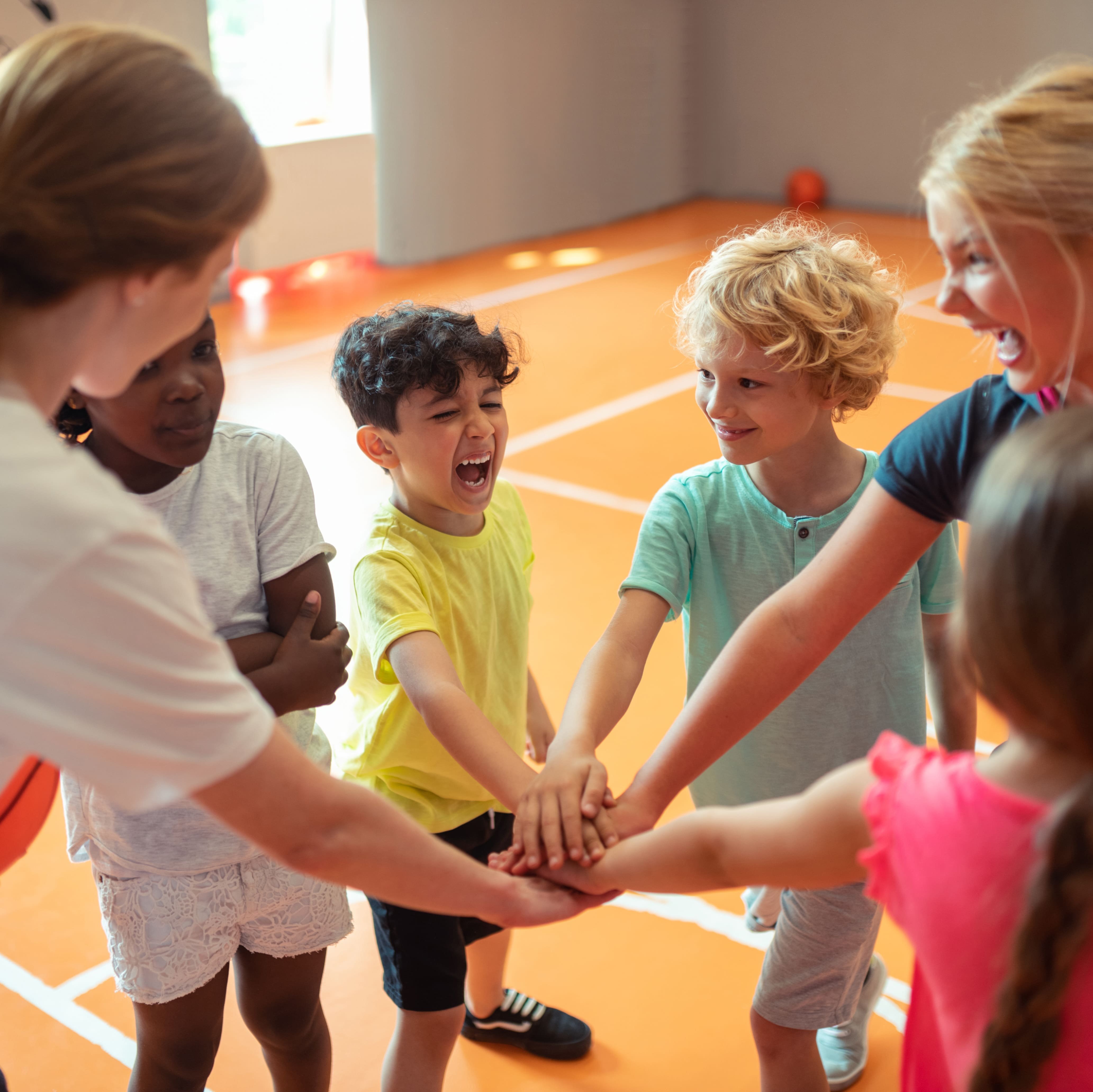 Arbeitsmaterial Sport zum Thema Bewegungsanreize Kinder stehen im Kreis und strecken ihre Arme in die Mitte