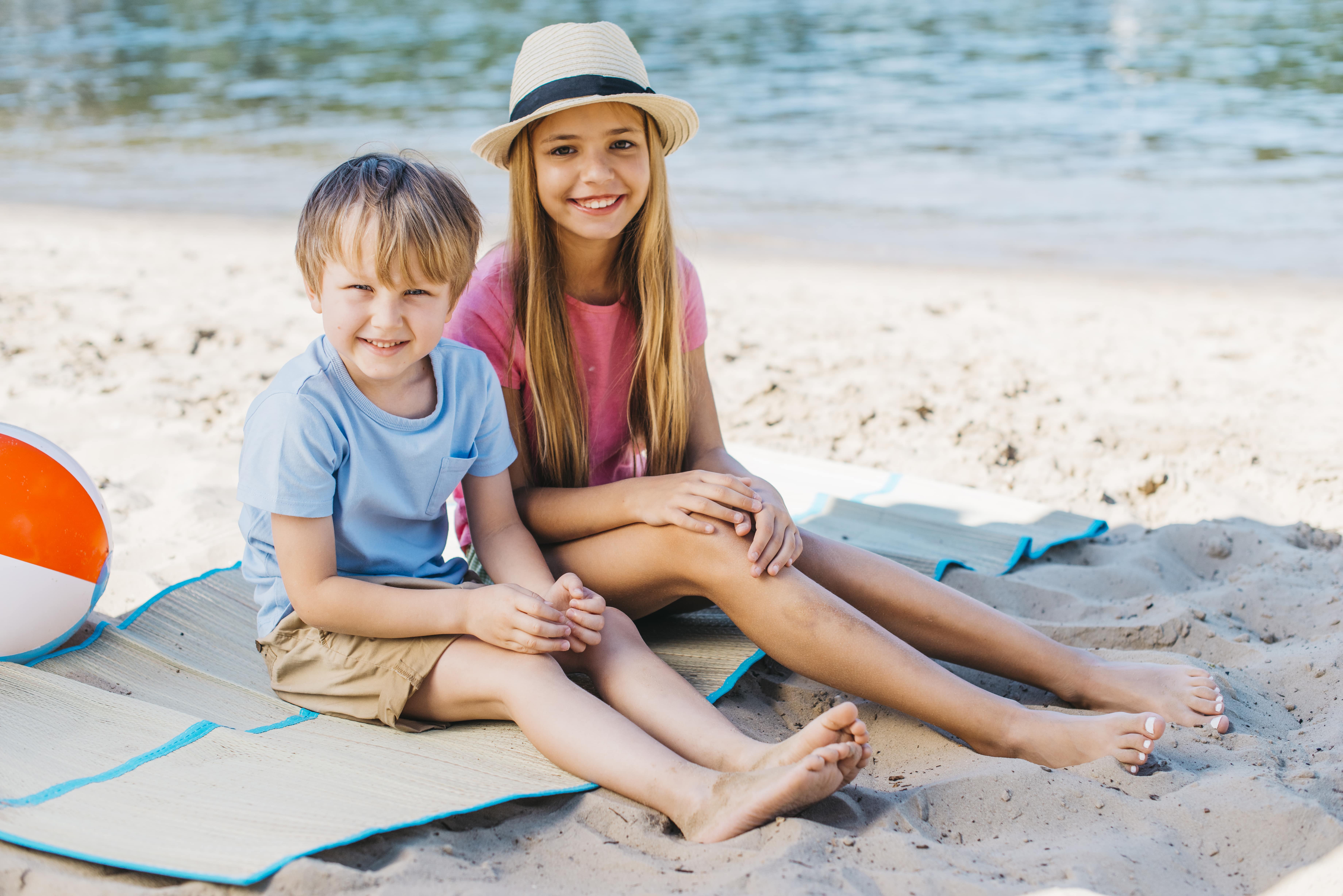 Kinder sitzen am Strand in sommerlichen Klamotten